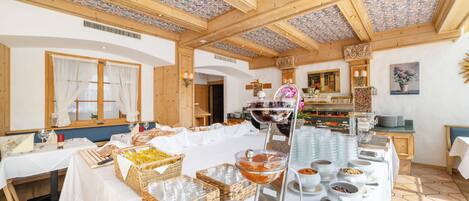 Una mesa de buffet con diferentes alimentos y bebidas, vigas de madera en el techo y una ventana con cortinas.