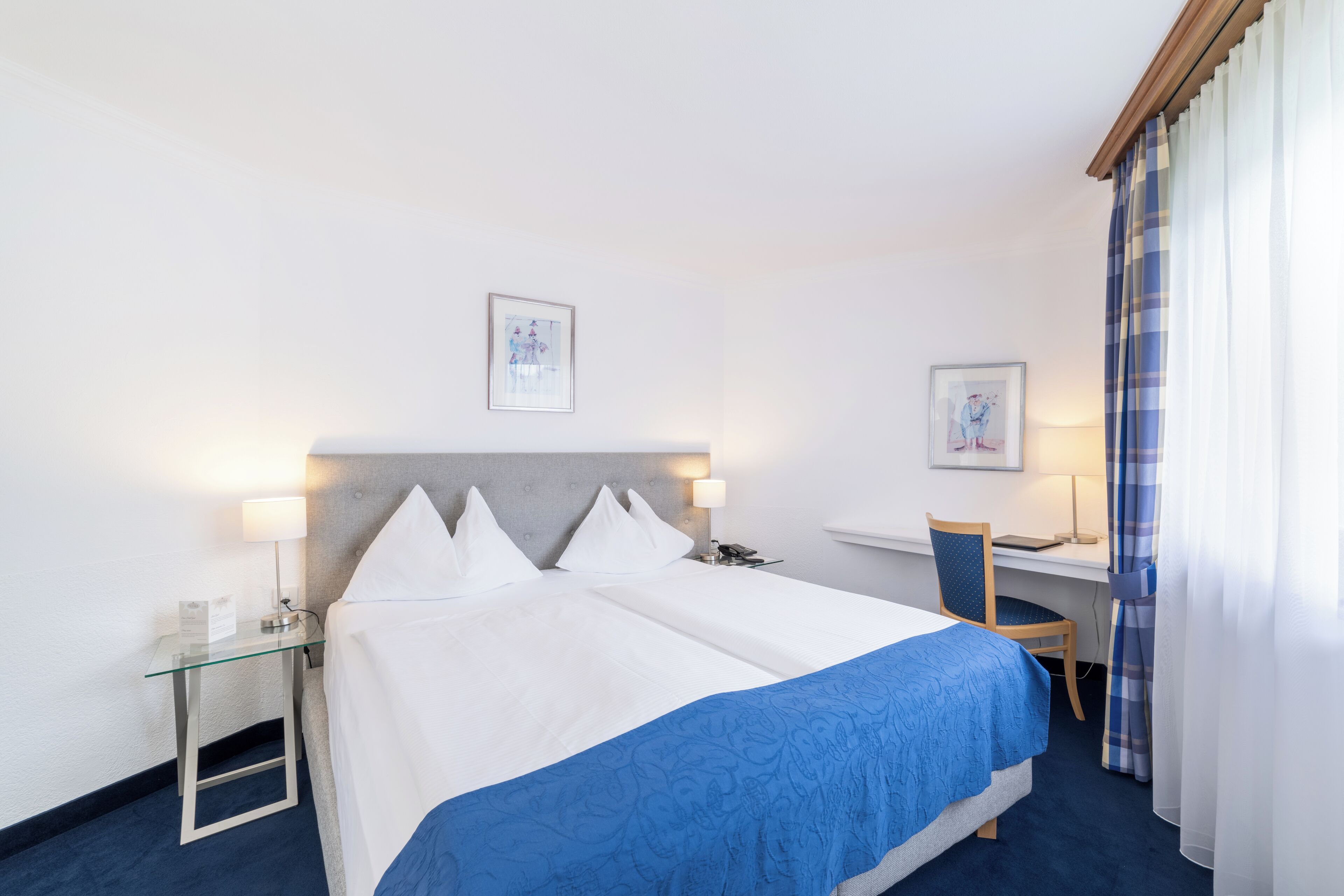 A hotel room with a bed, a desk, a chair, and two wall-mounted lamps.