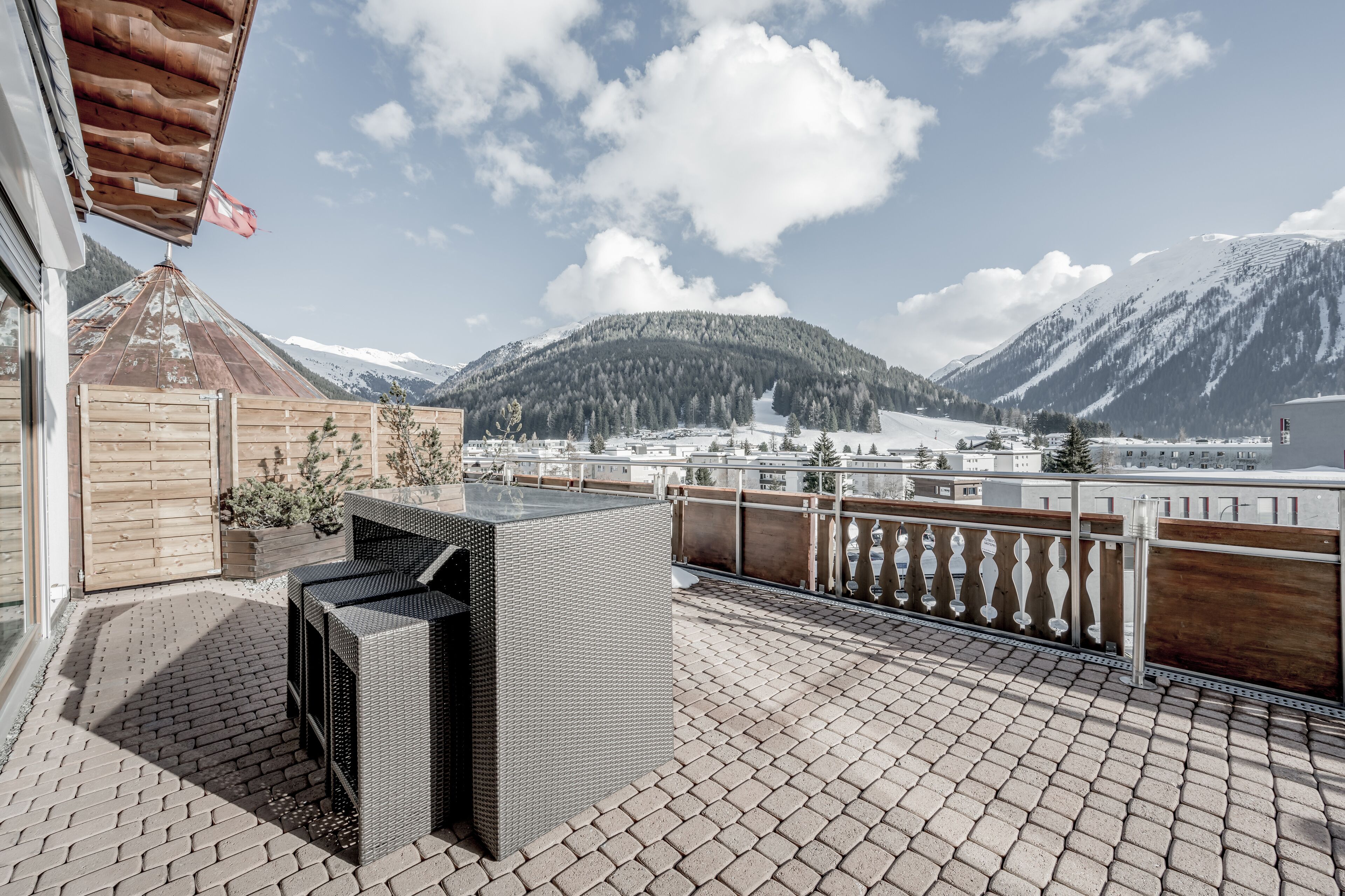 A patio with wicker furniture, a wooden fence, and a view of snow-covered mountains.