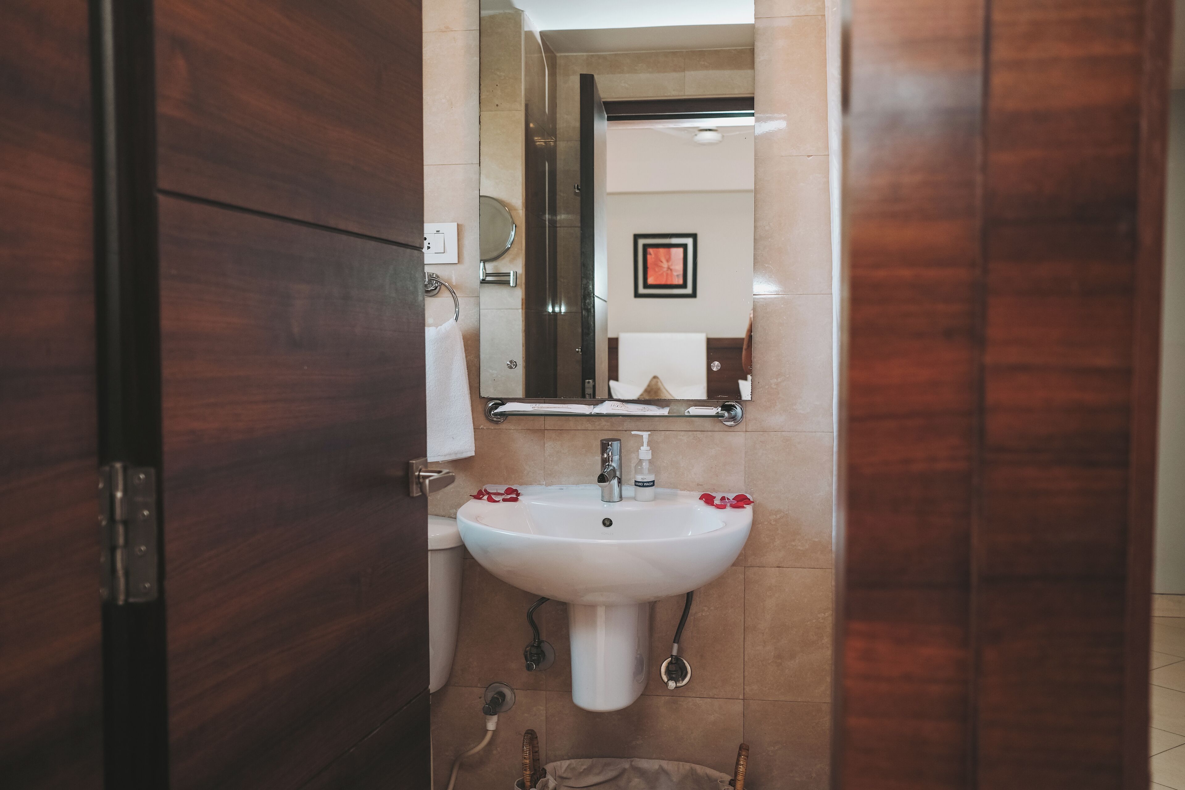 Un baño con lavamanos blanco, un espejo y un perchero para toallas.