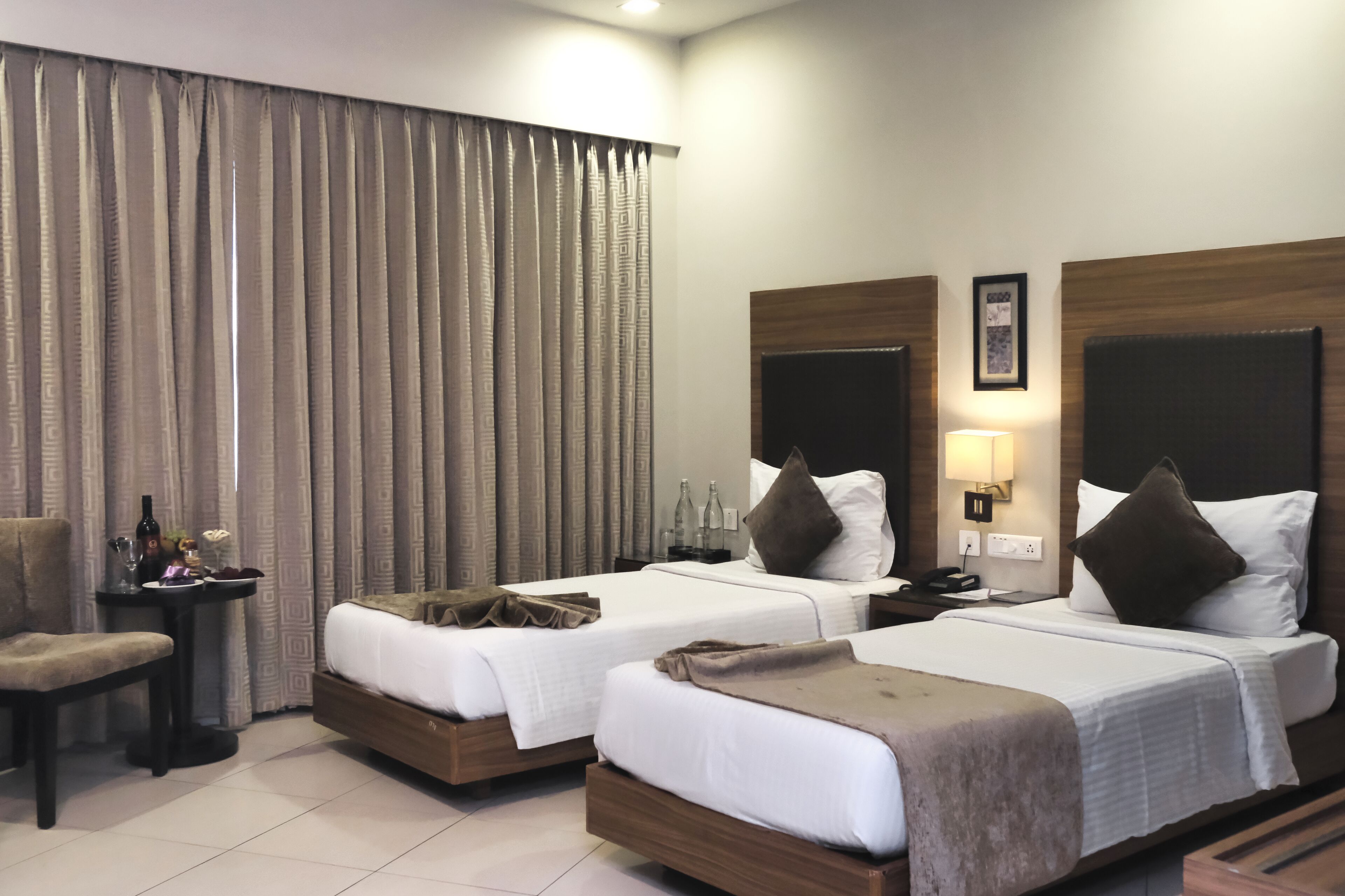 Habitación de hotel con dos camas, una mesita con una silla, una lámpara y un cuadro en la pared.
