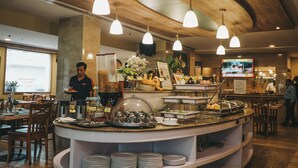 A buffet area with a variety of food items, a waiter serving, and a TV screen in the background.