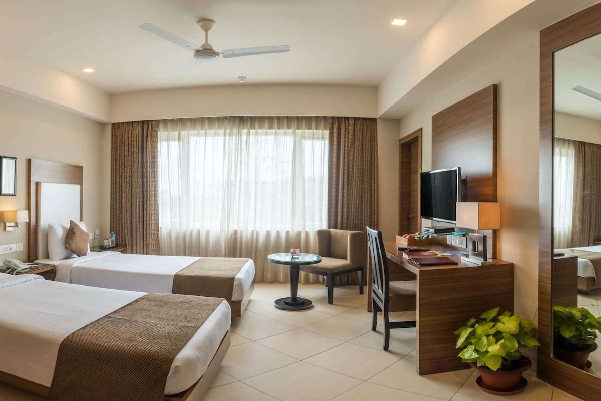 A hotel room with two beds, a desk, a chair, a TV, and a large mirror.