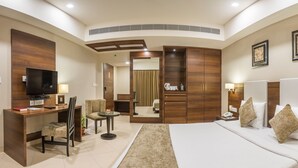 A modern hotel room with a large bed, a desk with a chair, a television, and a mirror.