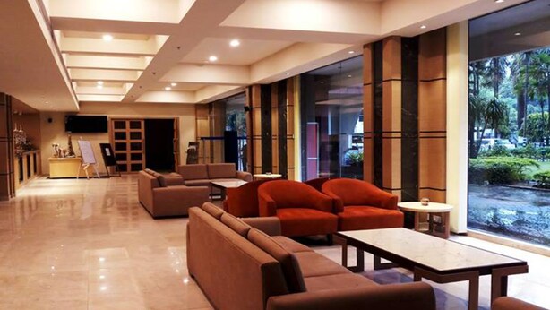 A modern hotel lobby with a seating area, a reception desk, and a large window offering a view of greenery.