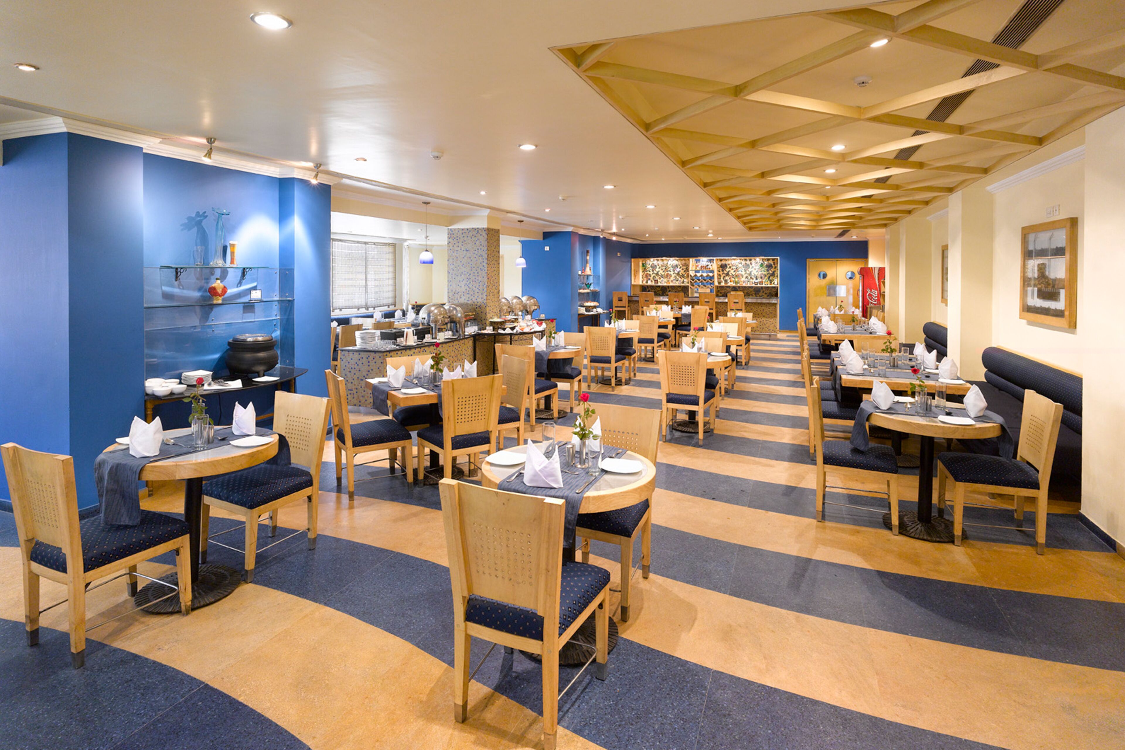 Un restaurante espacioso con varias zonas de comedor, muebles de madera y un suelo a rayas azul y amarillo.