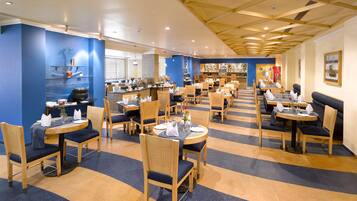 Un restaurante espacioso con varias zonas de comedor, muebles de madera y un suelo a rayas azul y amarillo.