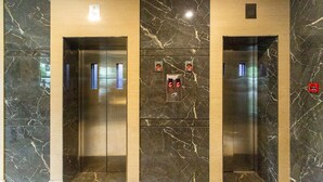 A set of three elevators with marble walls and a central control panel.
