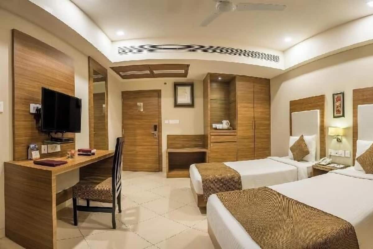 A hotel room with two beds, a desk, a TV, and a bathroom.