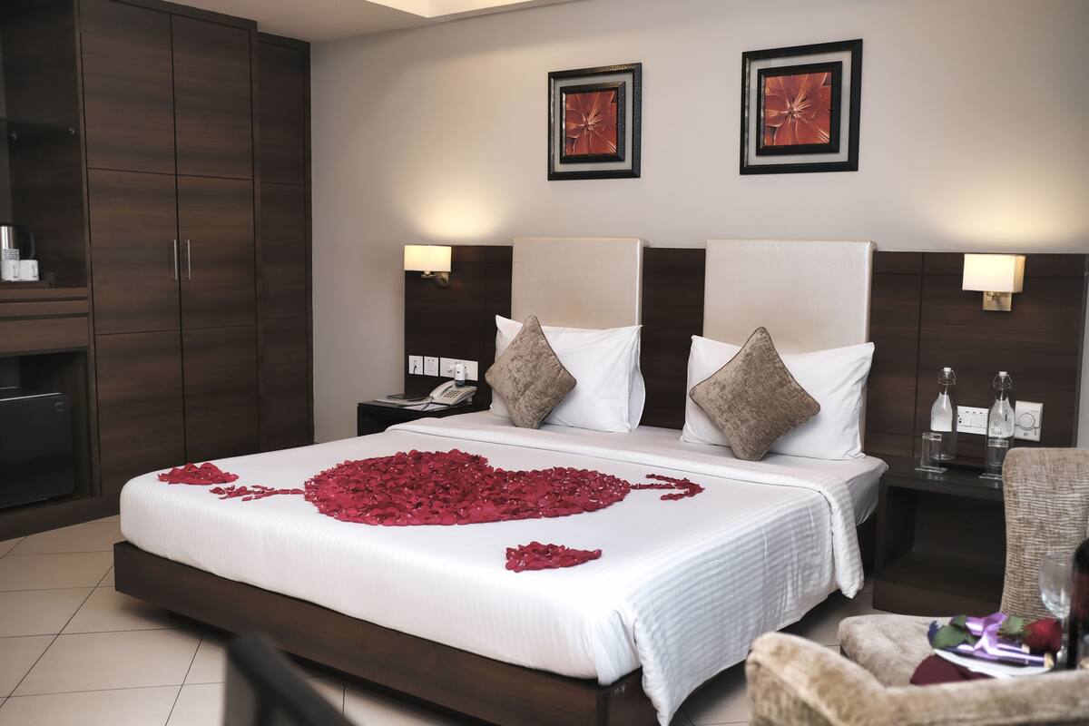 A hotel room with a large bed, two bedside tables, a wardrobe, and two framed pictures on the wall.