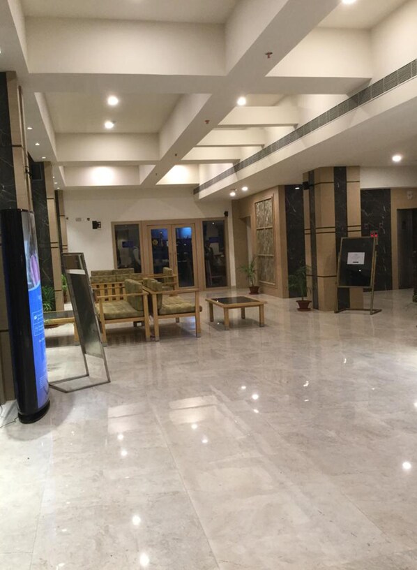 Un vestíbulo amplio con techo alto, iluminación empotrada, una mesa de recepción y una zona de estar con sillas y una mesa.