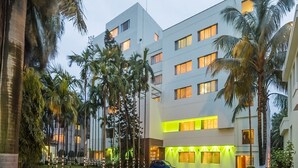 A modern hotel with multiple floors, a parking area, and palm trees.