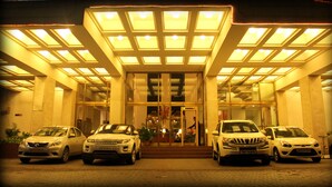A hotel entrance with three cars parked in front, a glass facade, and a person standing near the entrance. - Hotel Sagar Plaza (Pune)