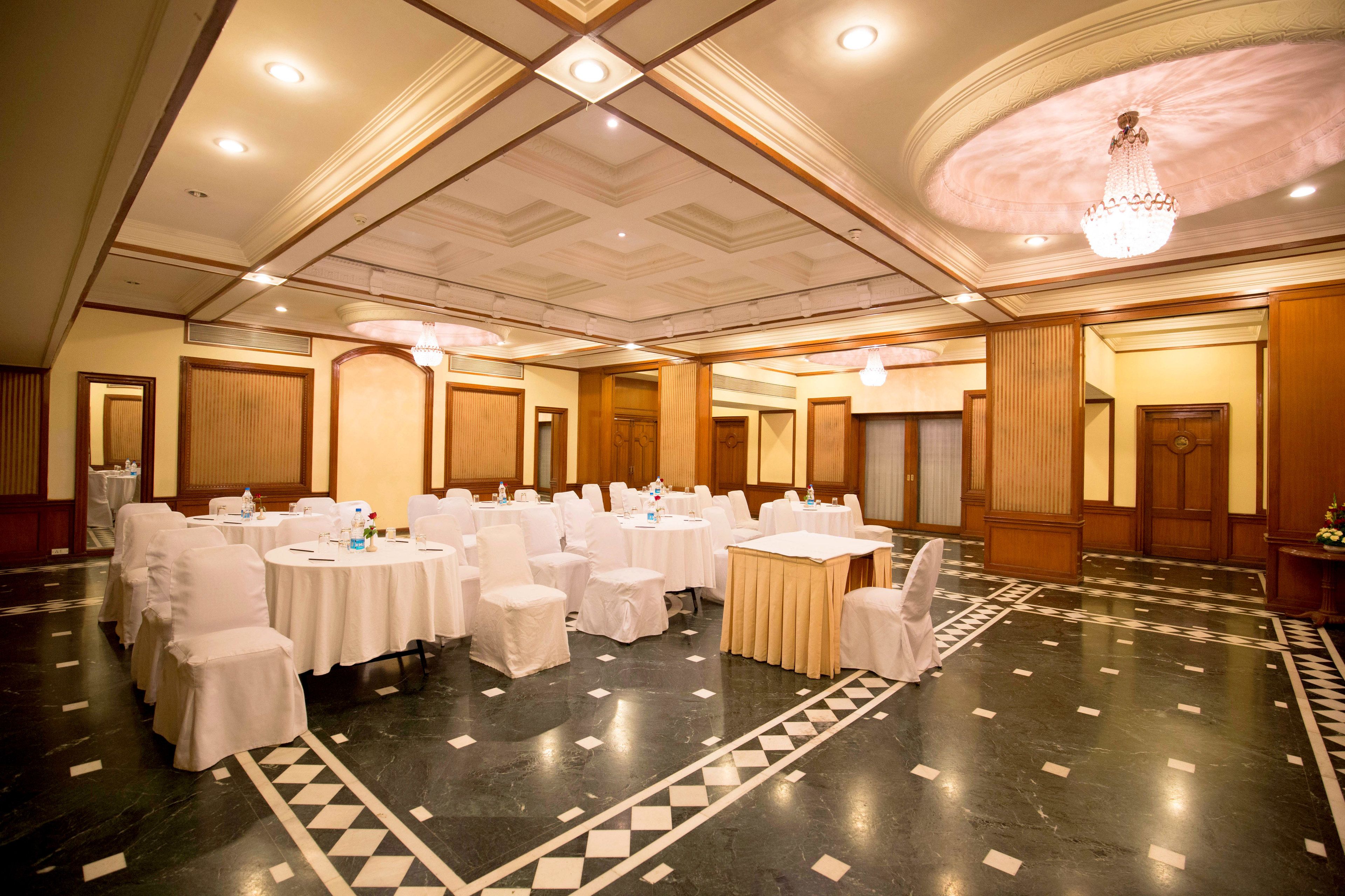 A banquet hall with round tables, white chairs, and a chandelier.