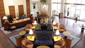A lobby with a reception desk, seating area with armchairs and a sofa, and a large window with a view of the outside. - Hotel Sagar Plaza (Pune)