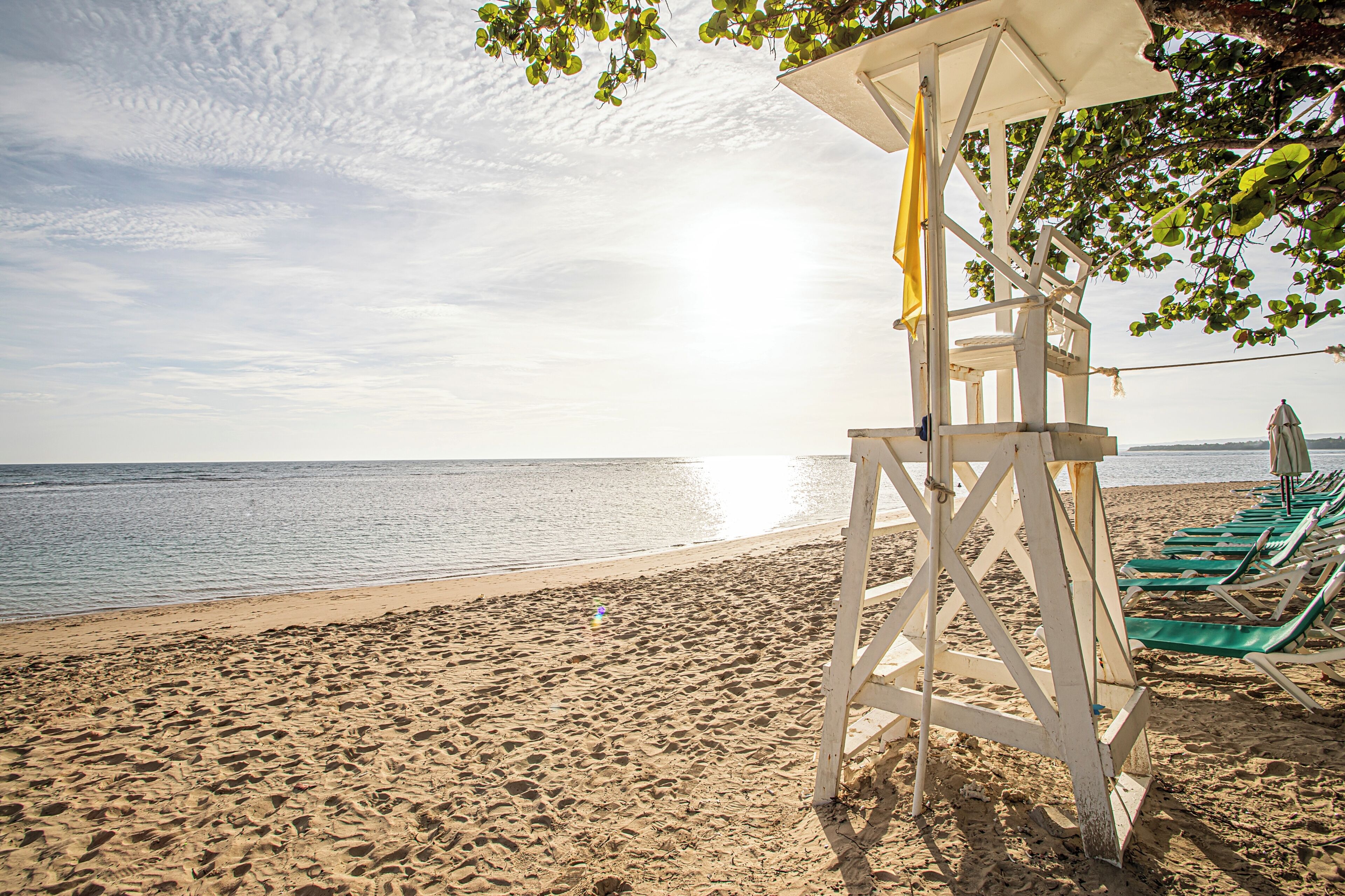 A beach with a lifeguard tower, green lounge chairs, and a clear view of the ocean.