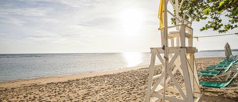 A beach with a lifeguard tower, green lounge chairs, and a clear view of the ocean.