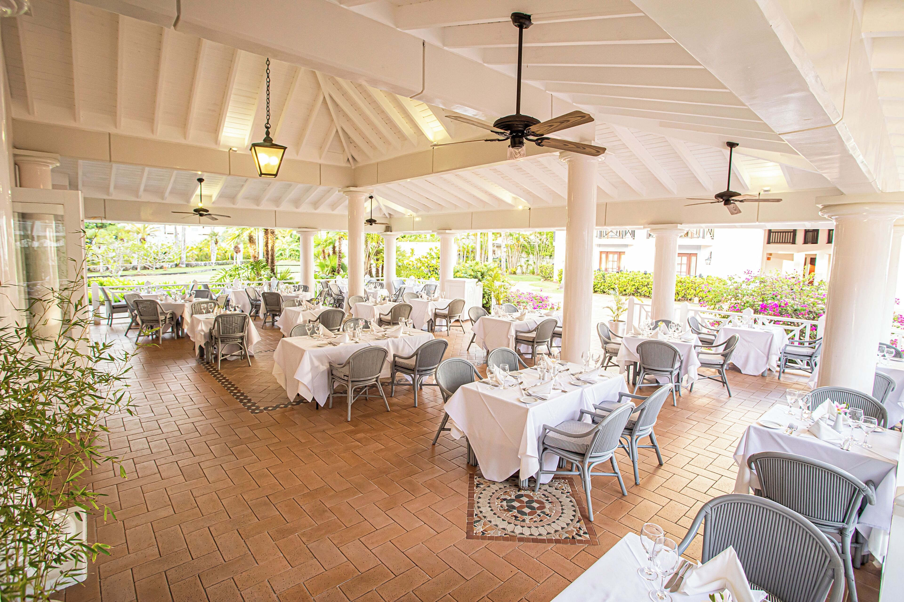 A covered outdoor dining area with tables and chairs, ceiling fans, and hanging lights.