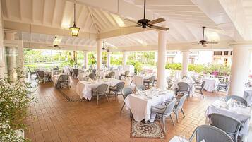 A covered outdoor dining area with tables and chairs, ceiling fans, and hanging lights.