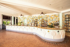 A spacious lobby with a curved reception desk, ceiling fans, and a tiled wall with a geometric pattern.
