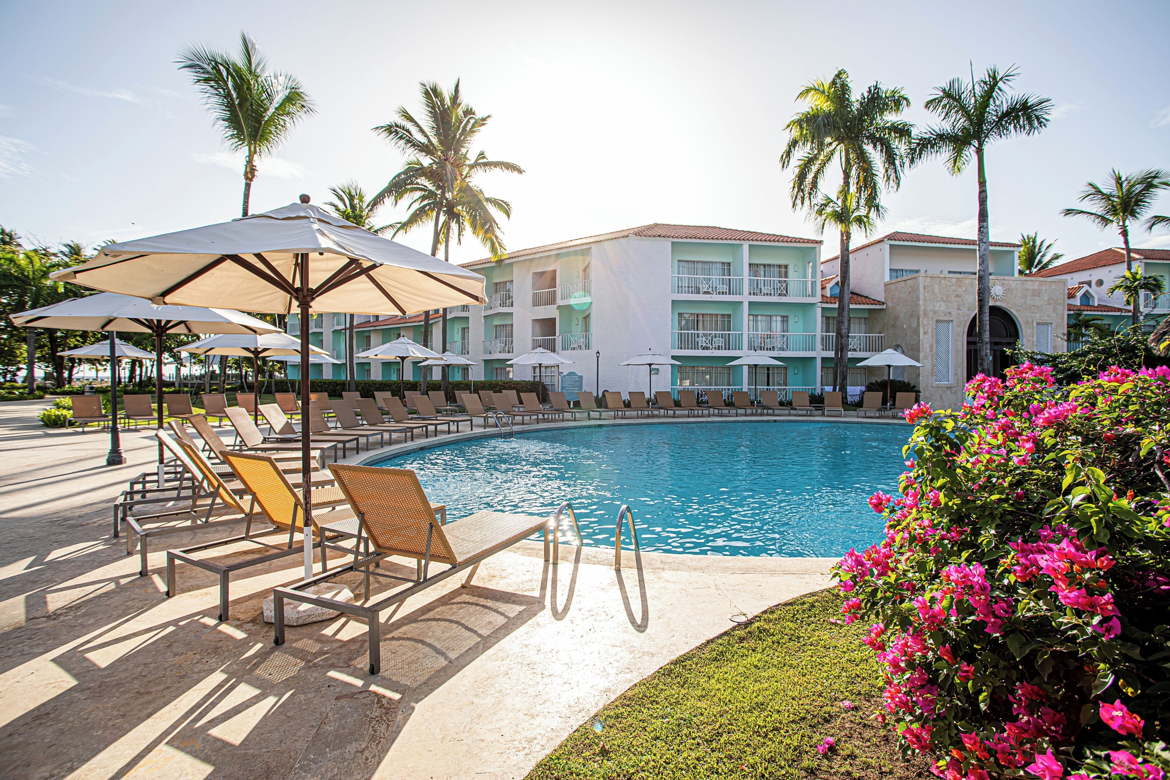 A poolside area with lounge chairs, umbrellas, and a building with balconies.