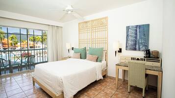 A hotel room with a bed, desk, chair, and a view of the pool area.