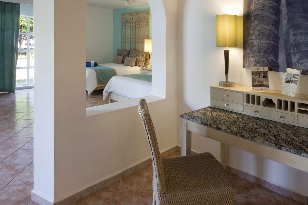 A hotel room with a bed, a desk, a chair, a lamp, and a large mirror.