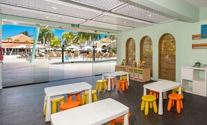 A children's play area with tables and stools, a pool view, and a reception desk with a sign.