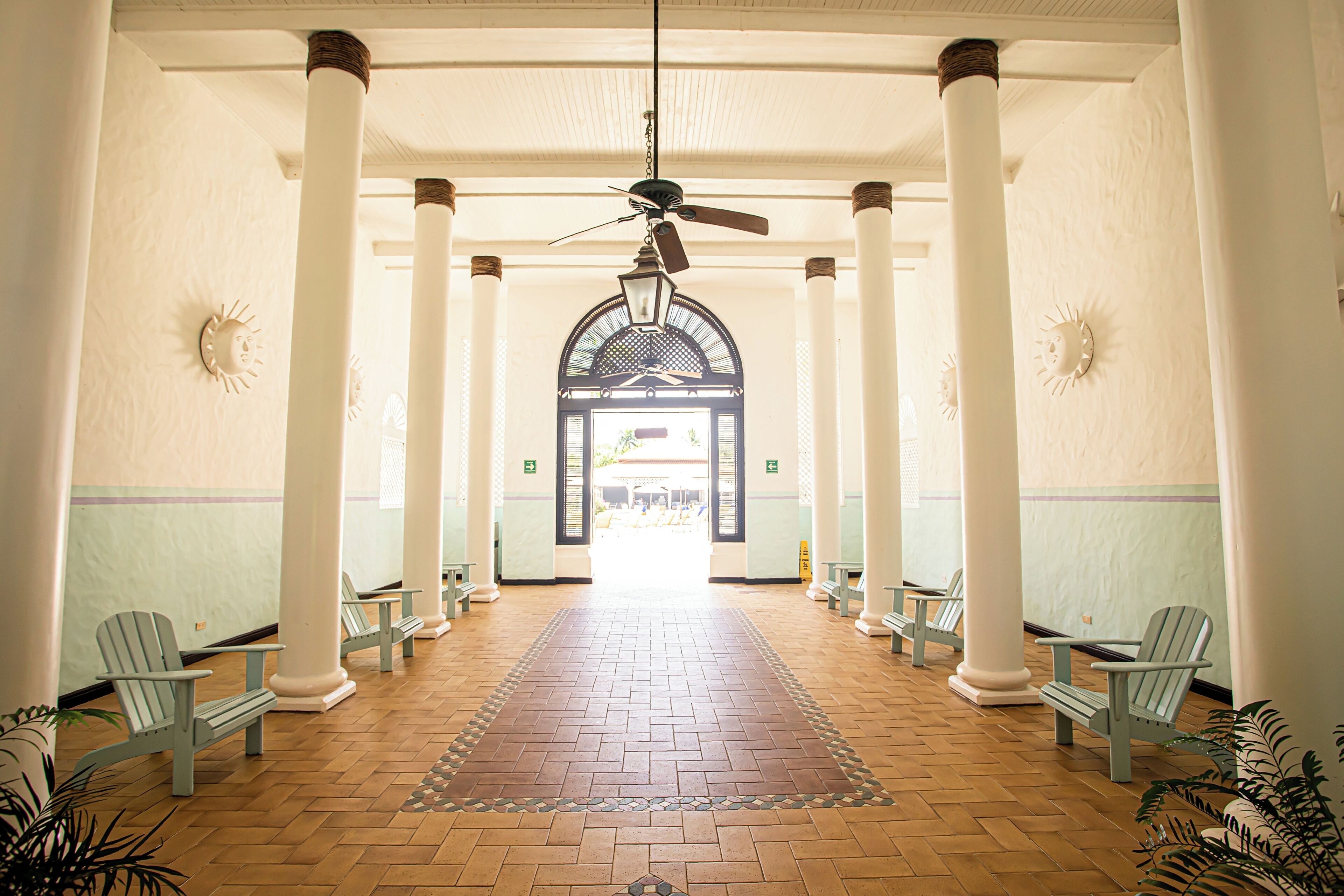 A corridor with white columns, a ceiling fan, and a patterned rug leading to an arched doorway.