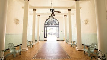 A corridor with white columns, a ceiling fan, and a patterned rug leading to an arched doorway.