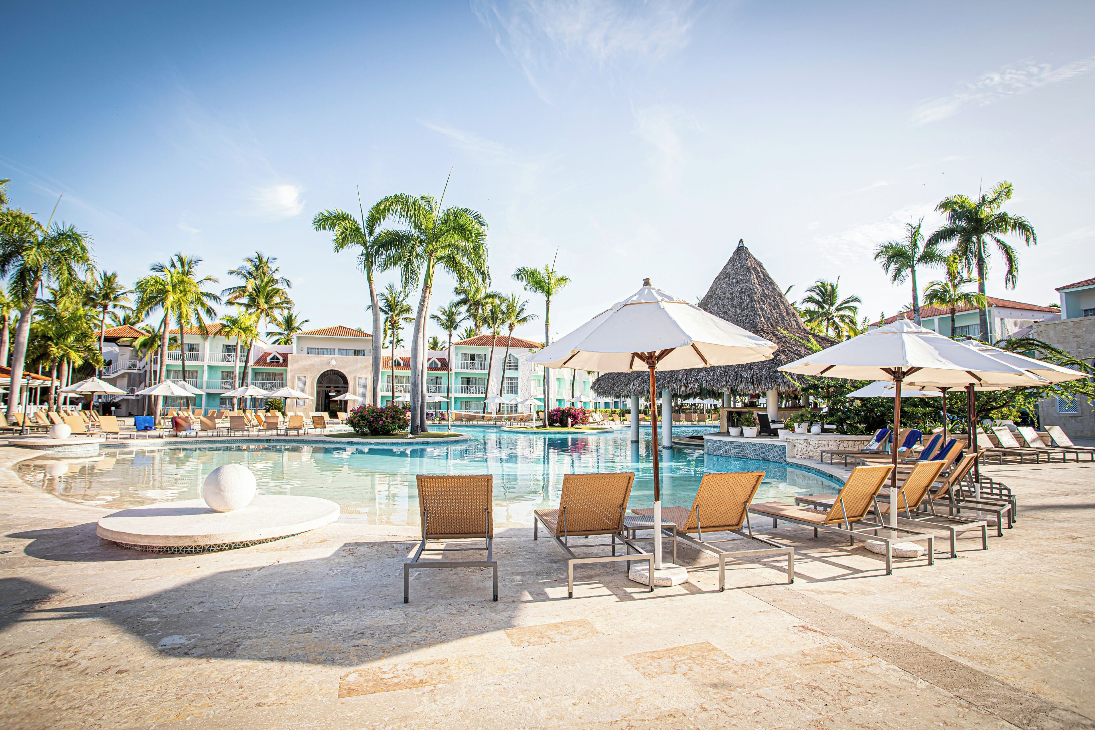 A resort pool area with lounge chairs, umbrellas, and palm trees.