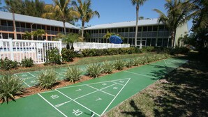 A shuffleboard court with a white fence and palm trees in the background. - Silver Sands Gulf Beach Resort by RVA (Longboat Key)