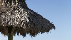 A wooden bench and a thatched umbrella on a sandy beach with a view of the ocean. - Silver Sands Gulf Beach Resort by RVA (Longboat Key)