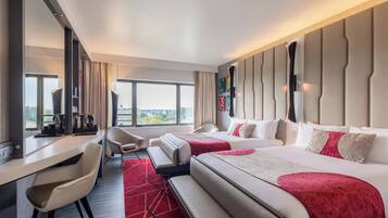 A hotel room with two beds, a desk, a chair, and a view of the city.