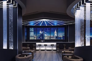 A modern bar area with a cityscape view, bar stools, and a unique ceiling design.