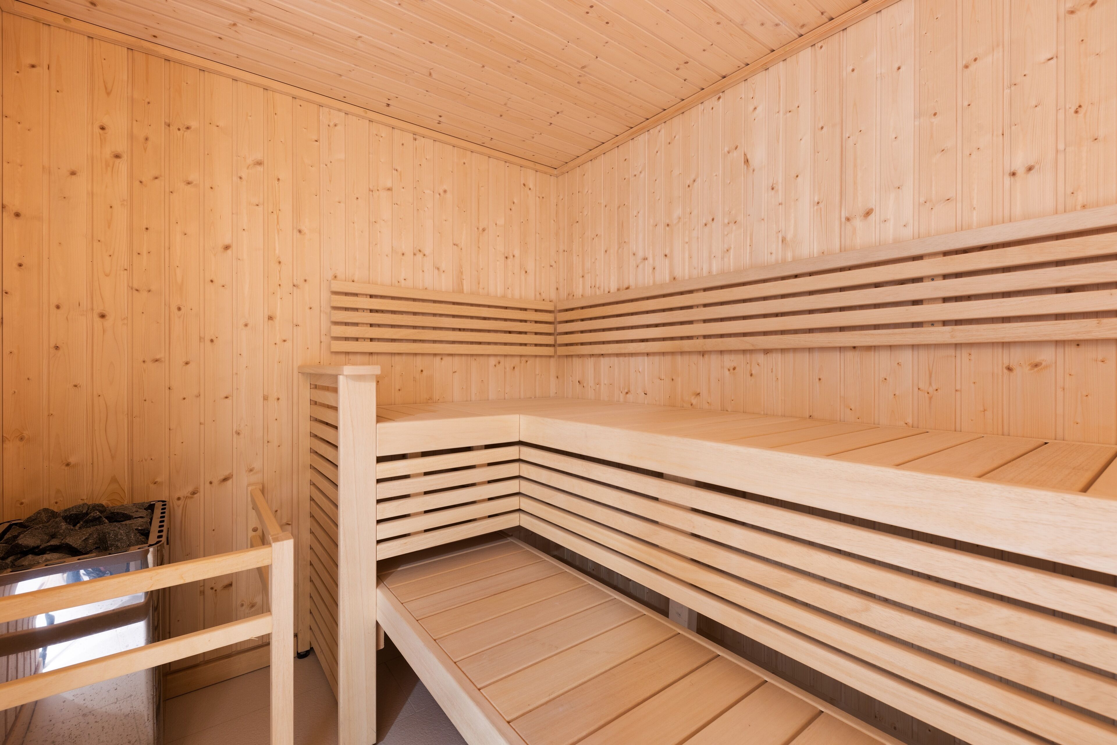 A sauna with wooden benches and a metal container for rocks.
