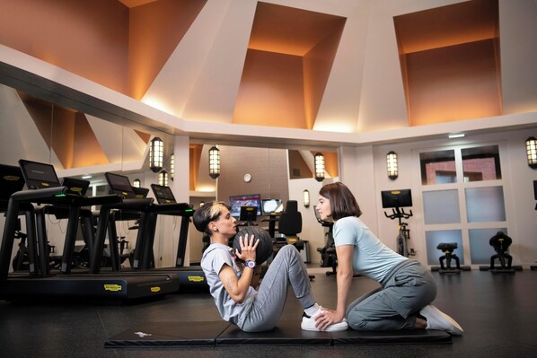A gym with treadmills, exercise balls, and a person performing a sit-up with another person. - Disney Hotel New York - The Art of Marvel (Chessy)