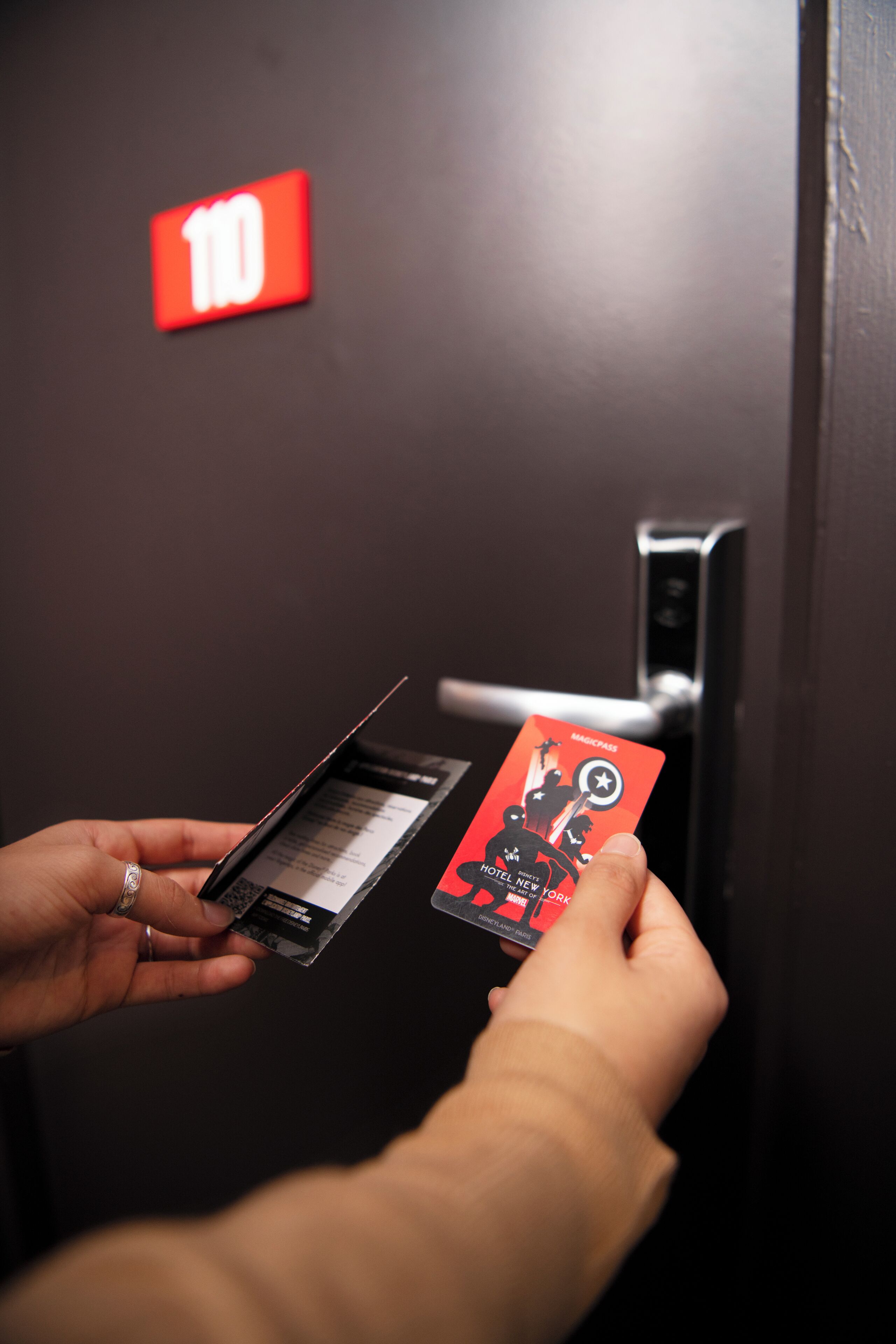 Una mano sostiene una tarjeta llave de hotel con un diseño rojo y negro, y una puerta con un letrero rojo que indica el número de habitación 10.