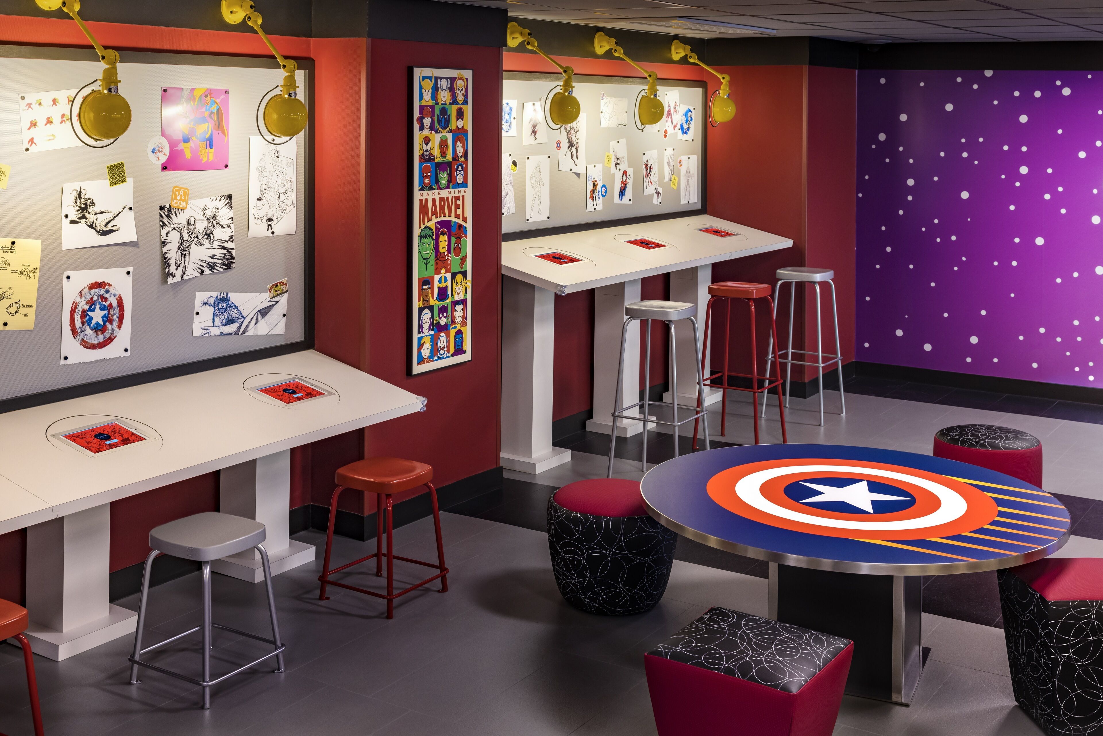 Une pièce avec une table blanche, des tabourets rouges et une table ronde ornée d’un motif représentant le bouclier de Captain America.