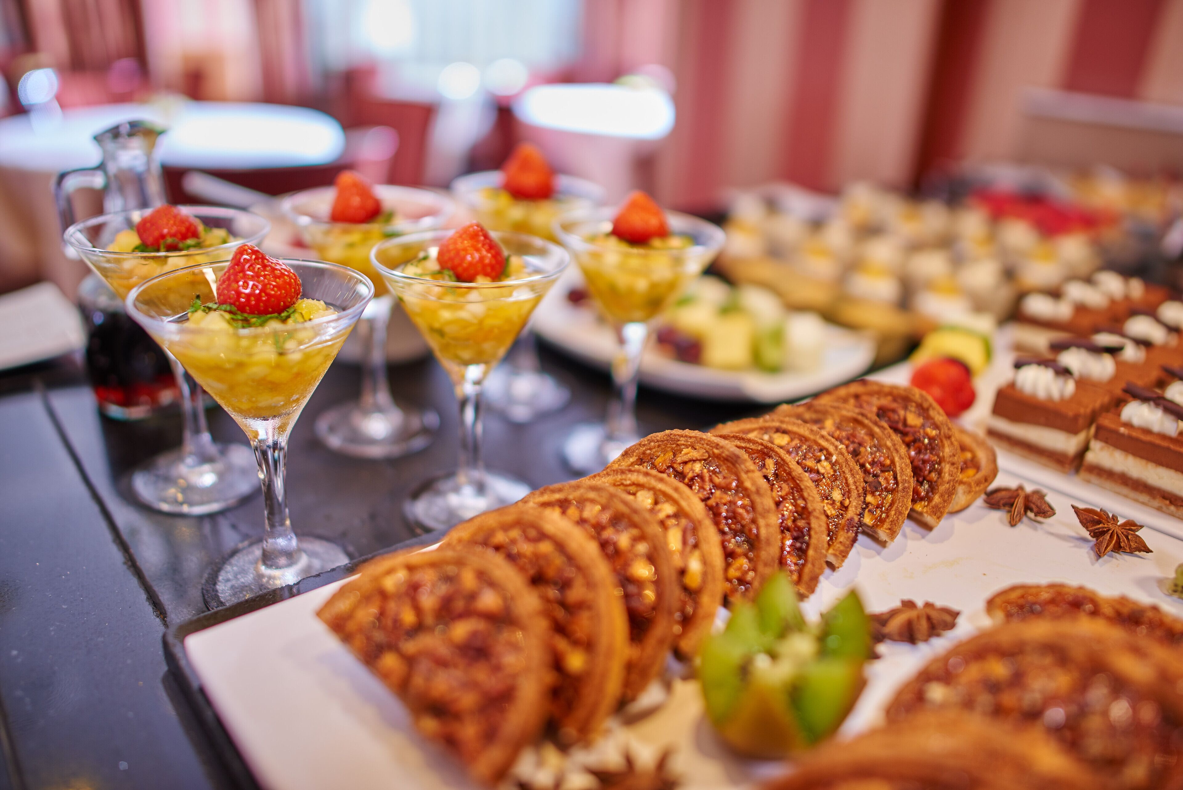 A variety of desserts and pastries on a table, including sliced pastries and a selection of fruit-topped drinks.