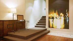 A staircase with carpeted steps leading to a landing, a wall-mounted lamp, and a framed picture on a small table.