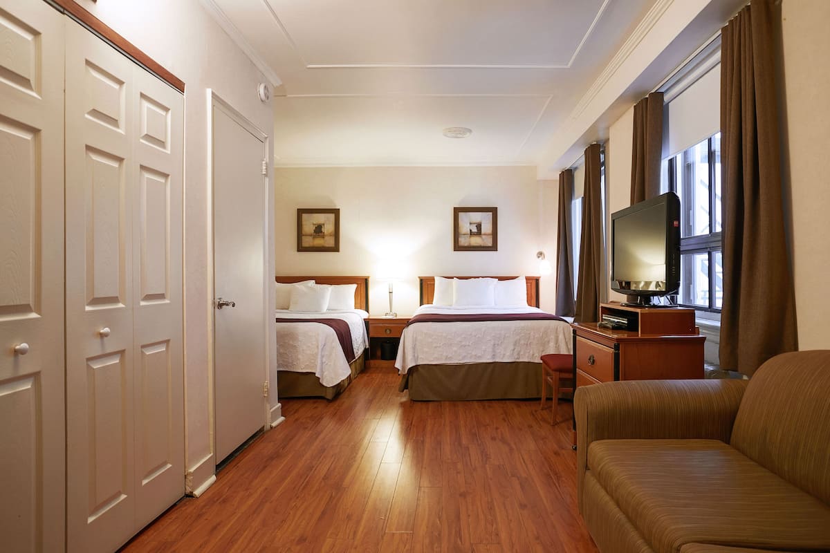 A hotel room with two beds, a television, and a sofa.