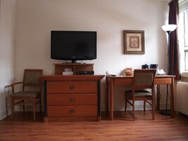 Habitación de hotel con un escritorio de madera, dos sillas, un televisor, un cuadro en la pared y una lámpara cerca de la ventana.