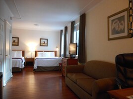 A hotel room with two beds, a sofa, a TV, and a desk with a lamp.