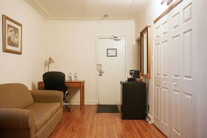A room with a brown sofa, a desk with a chair, a refrigerator, and a door with a mirror.