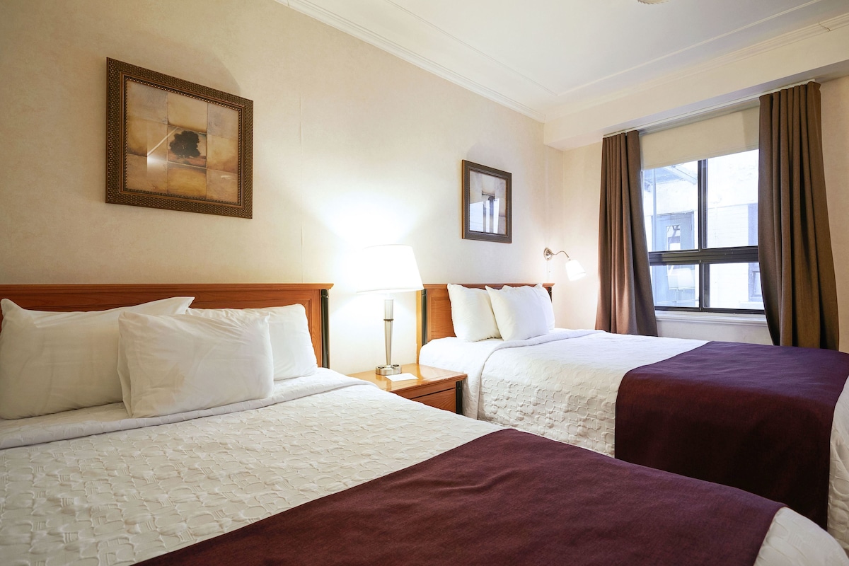A hotel room with two beds, a nightstand, a lamp, a framed picture, and a window with curtains.