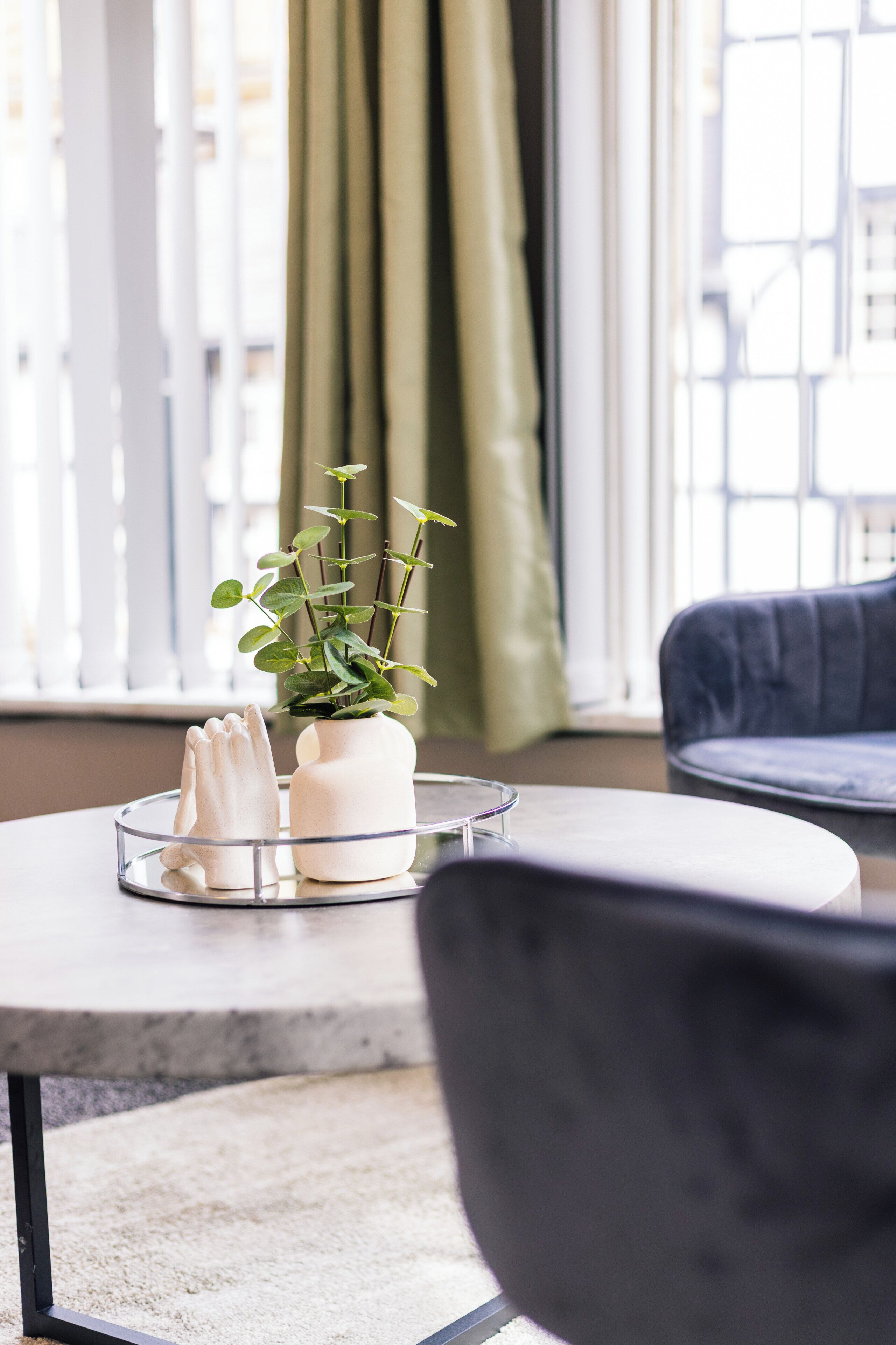 Une table ronde ornée d’une plante en pot et de deux vases blancs.