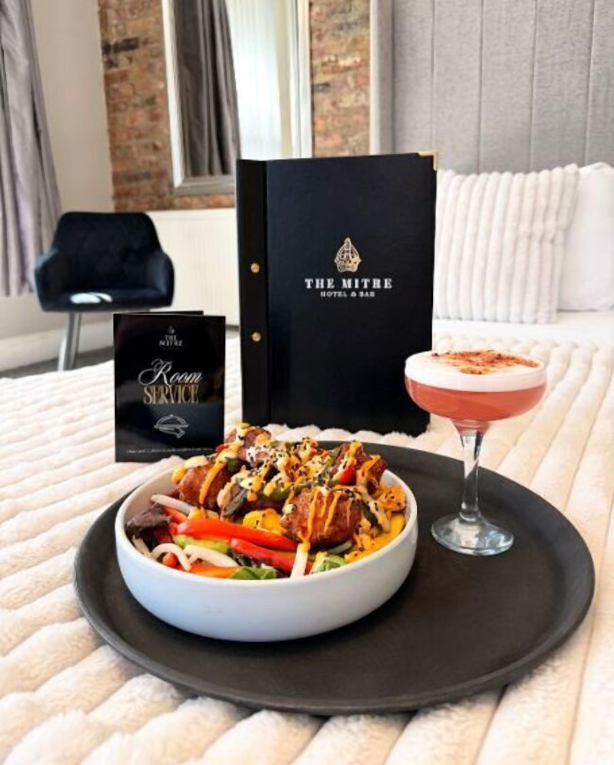 A room service menu, a bowl of food, and a cocktail on a tray.