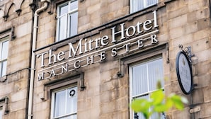 Um edifício histórico com a placa 'The Mitre Hotel Manchester', grandes janelas e arquitetura de pedra tradicional.