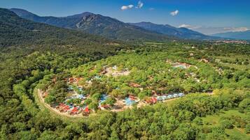 Vista aérea de un resort con varias construcciones rodeadas de un bosque denso y montañas al fondo.